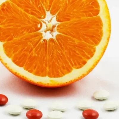 AdobeStock_20436586 (1) Half an orange, surrounded by vitamin and mineral supplement tablets.
