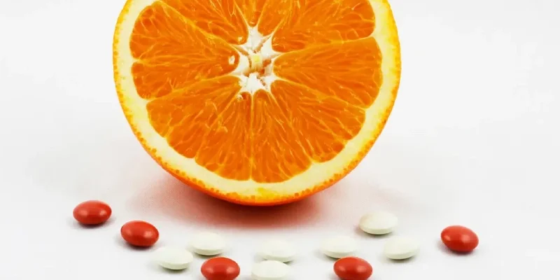 Half an orange, surrounded by vitamin and mineral supplement tablets.