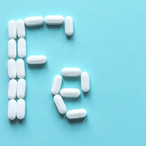AdobeStock_330672672 Next to an open pill bottle, several white tablets spell out ‘Fe’, the chemical symbol for iron