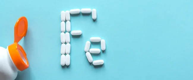 AdobeStock_330672672 Next to an open pill bottle, several white tablets spell out ‘Fe’, the chemical symbol for iron