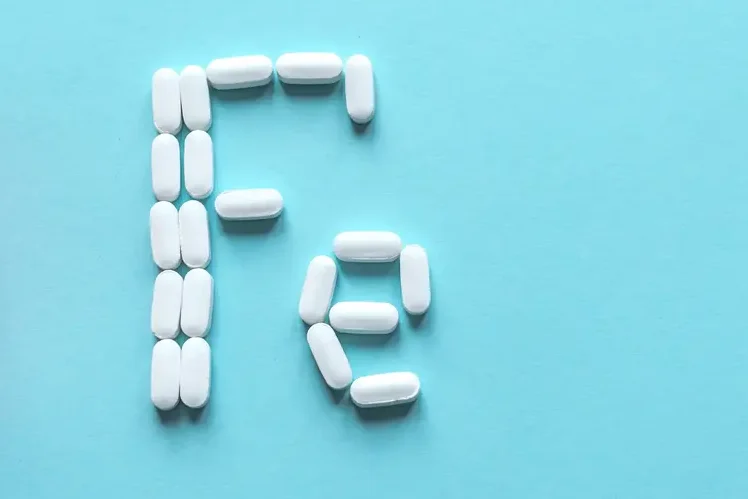 AdobeStock_330672672 Next to an open pill bottle, several white tablets spell out ‘Fe’, the chemical symbol for iron