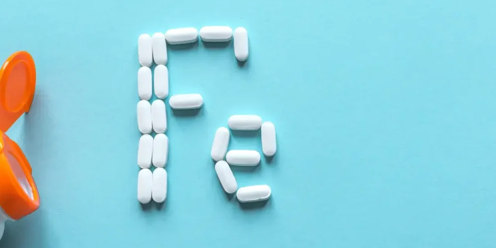 AdobeStock_330672672 Next to an open pill bottle, several white tablets spell out ‘Fe’, the chemical symbol for iron