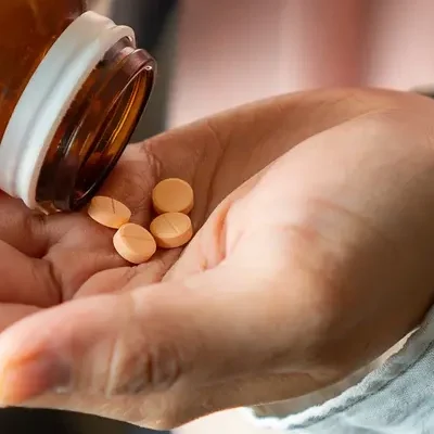 AdobeStock_893541409 Close-up of a woman shaking several supplement tablets out of a bottle into her hand.