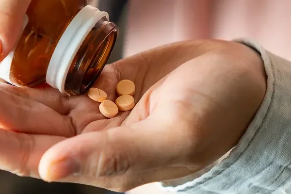 AdobeStock_893541409 Close-up of a woman shaking several supplement tablets out of a bottle into her hand.