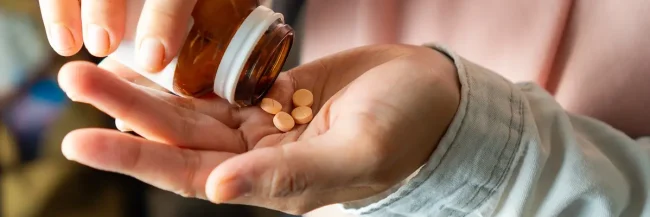 AdobeStock_893541409 Close-up of a woman shaking several supplement tablets out of a bottle into her hand.