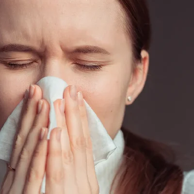 AdobeStock_3367627482 A young woman catches a sneeze in a tissue.