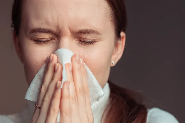 AdobeStock_3367627482 A young woman catches a sneeze in a tissue.