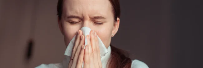 AdobeStock_3367627482 A young woman catches a sneeze in a tissue.