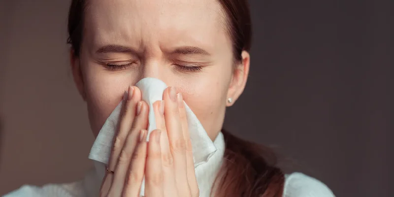 AdobeStock_3367627482 A young woman catches a sneeze in a tissue.