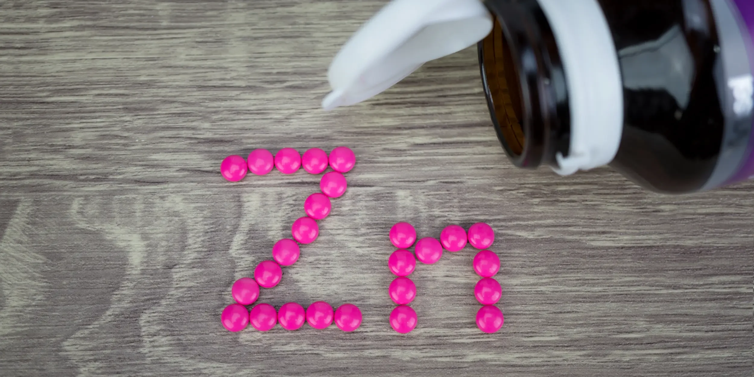 A selection of pink pills spelling out ‘Zn’, the chemical symbol for zinc, near an open pill bottle.