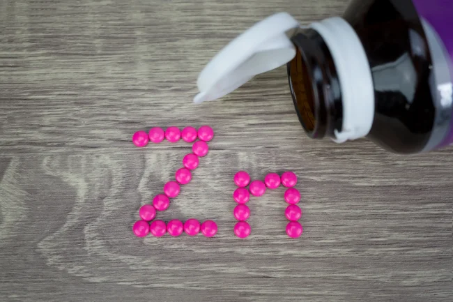 A selection of pink pills spelling out ‘Zn’, the chemical symbol for zinc, near an open pill bottle.