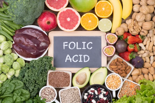 Examples of various healthy foods, including many that are rich in folate, surrounding a chalkboard reading ‘folic acid’.