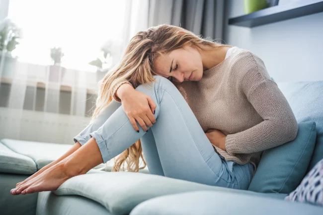 What are the most common side effects of folic acid A woman is in pain from a stomach ache, a possible side effect of folic acid supplements, while sitting on her sofa.