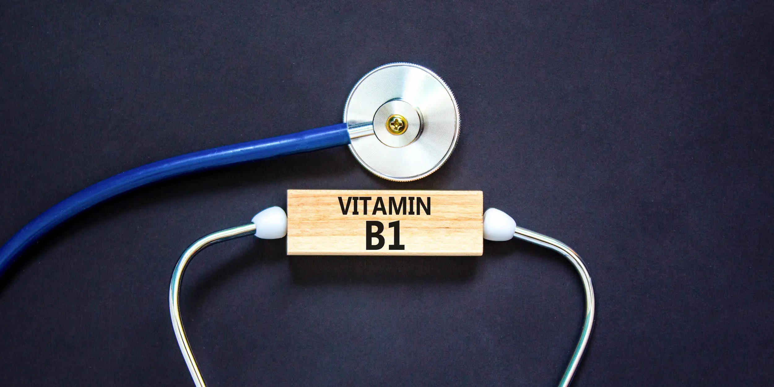 A wooden block reading ‘vitamin B1’ is surrounded by a stethoscope, indicating the nutrient’s role in supporting heart health.