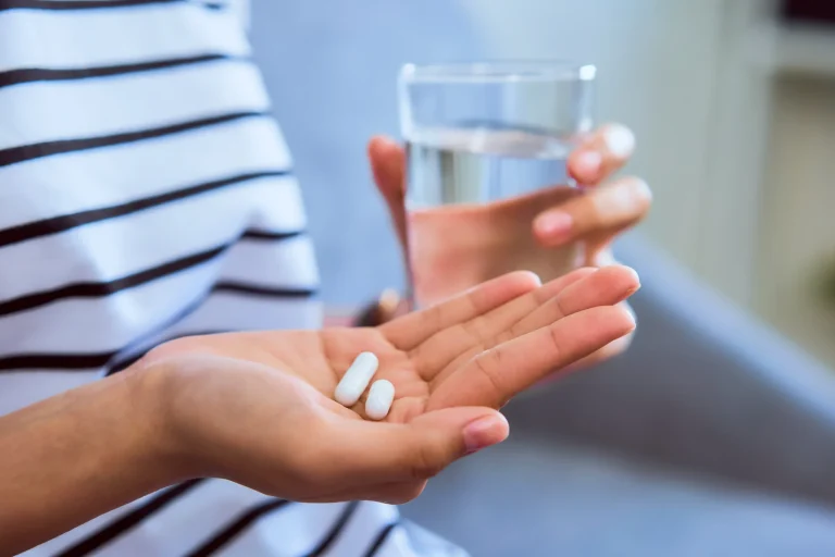 What is a Food Supplement A woman holds two tablets in one hand and a glass of water in the other.