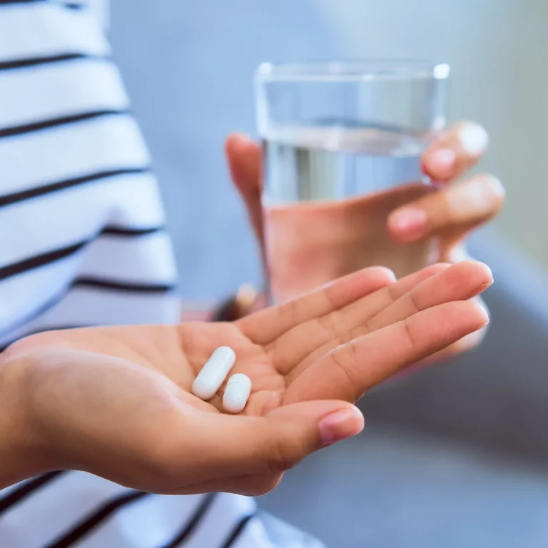 What is a Food Supplement A woman holds two tablets in one hand and a glass of water in the other.