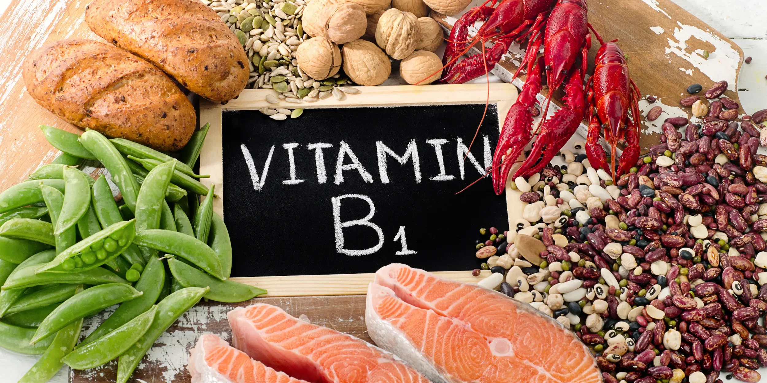 A selection of healthy foods including sources of thiamin, surrounding a chalkboard that reads ‘vitamin B1’.
