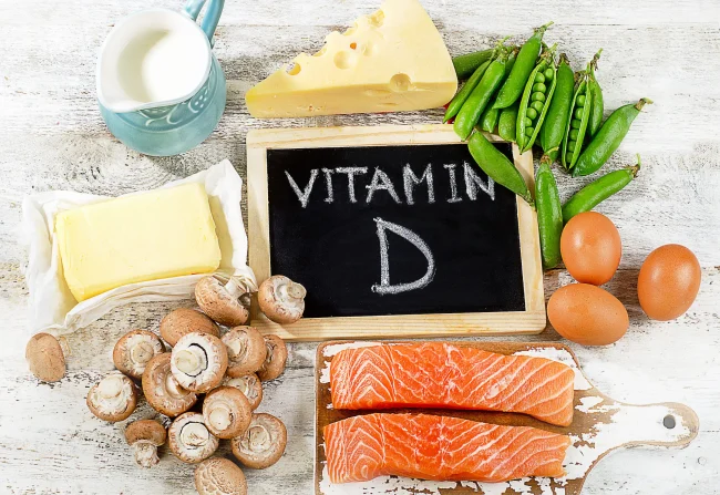 A spread of healthy foods, including some that are high in vitamin D, around a chalkboard that reads ‘vitamin D’.