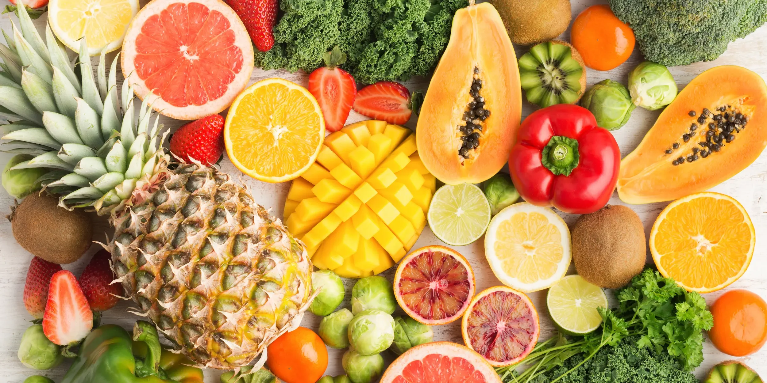 A selection of fruits and vegetables high in vitamin C laid out on a white background.
