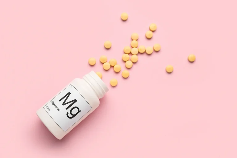 Why Take Magnesium Supplements A bottle of pills spilling across a pink background. The bottle is labelled ‘Mg’ for magnesium.