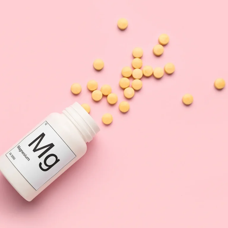 Why Take Magnesium Supplements A bottle of pills spilling across a pink background. The bottle is labelled ‘Mg’ for magnesium.