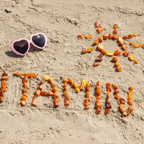 Amber sea glass spells out ‘Vitamin D’ and an image of a sun on a beach next to a pair of pink heart-shaped sunglasses.
