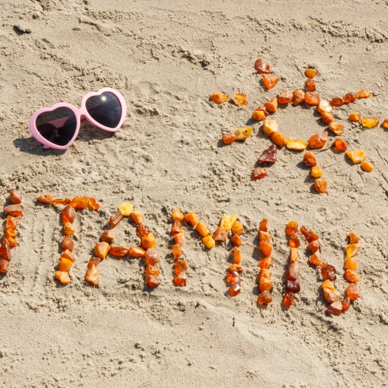 Amber sea glass spells out ‘Vitamin D’ and an image of a sun on a beach next to a pair of pink heart-shaped sunglasses.