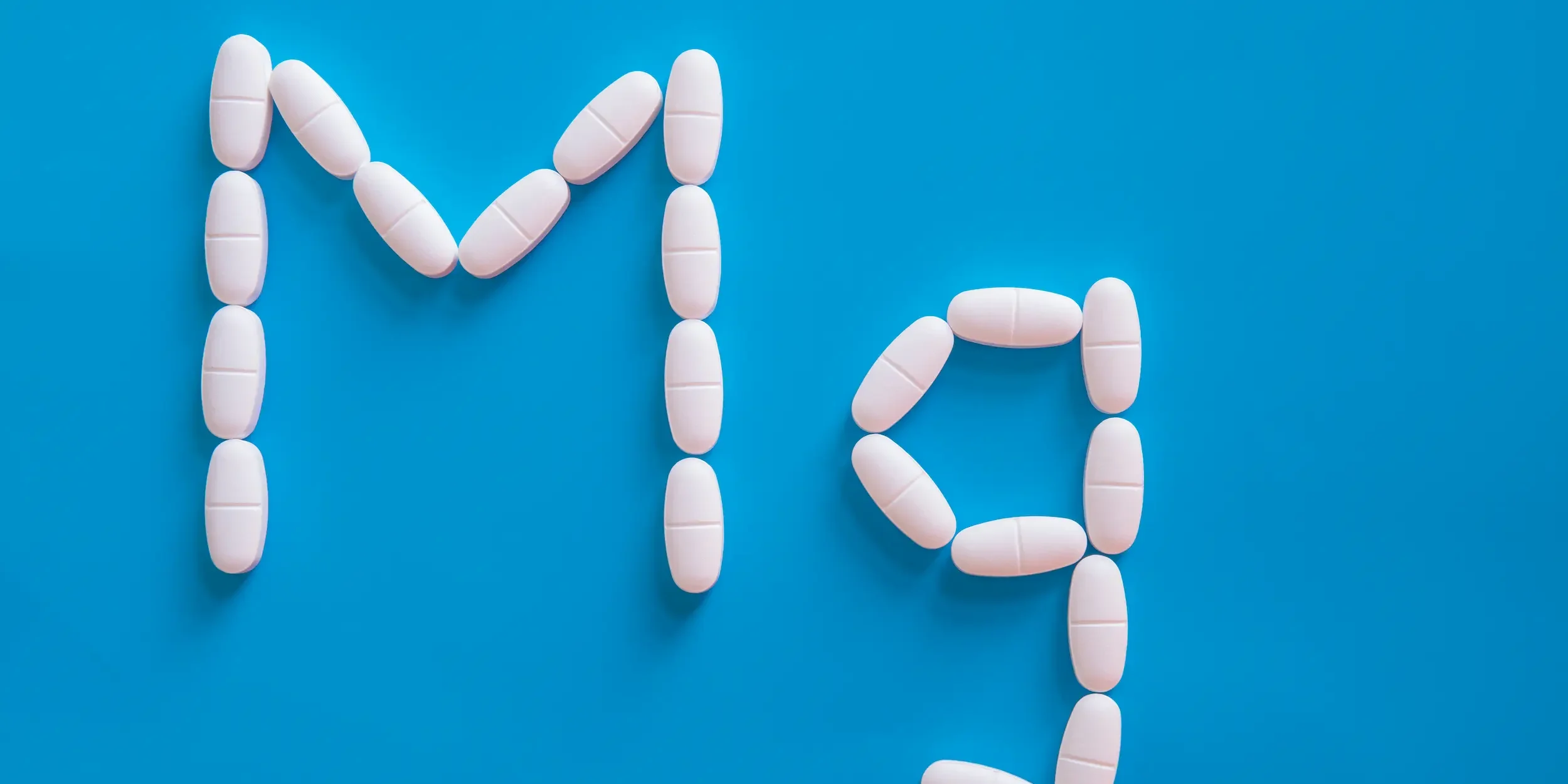 Do magnesium supplements have any side effects Small white pills spell out ‘Mg’, the chemical symbol for magnesium, on a blue background.