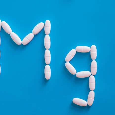 Small white pills spell out ‘Mg’, the chemical symbol for magnesium, on a blue background.