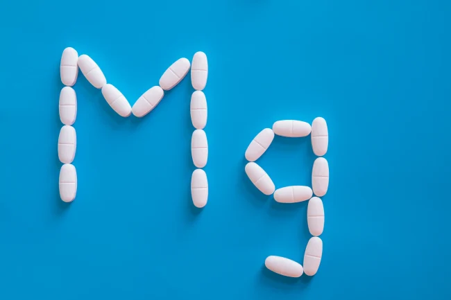 Small white pills spell out ‘Mg’, the chemical symbol for magnesium, on a blue background.