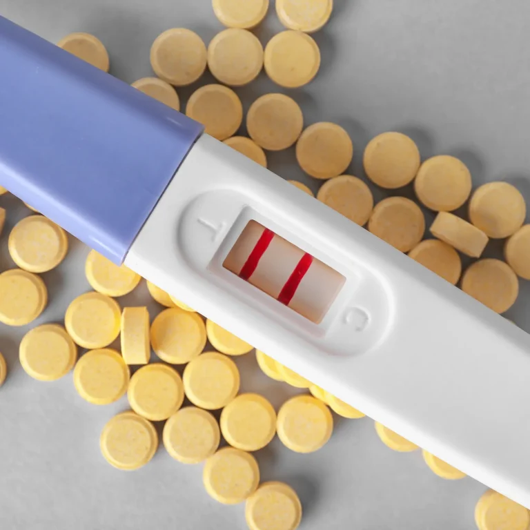 A positive pregnancy test on top of small yellow pills, representing folic acid supplements.