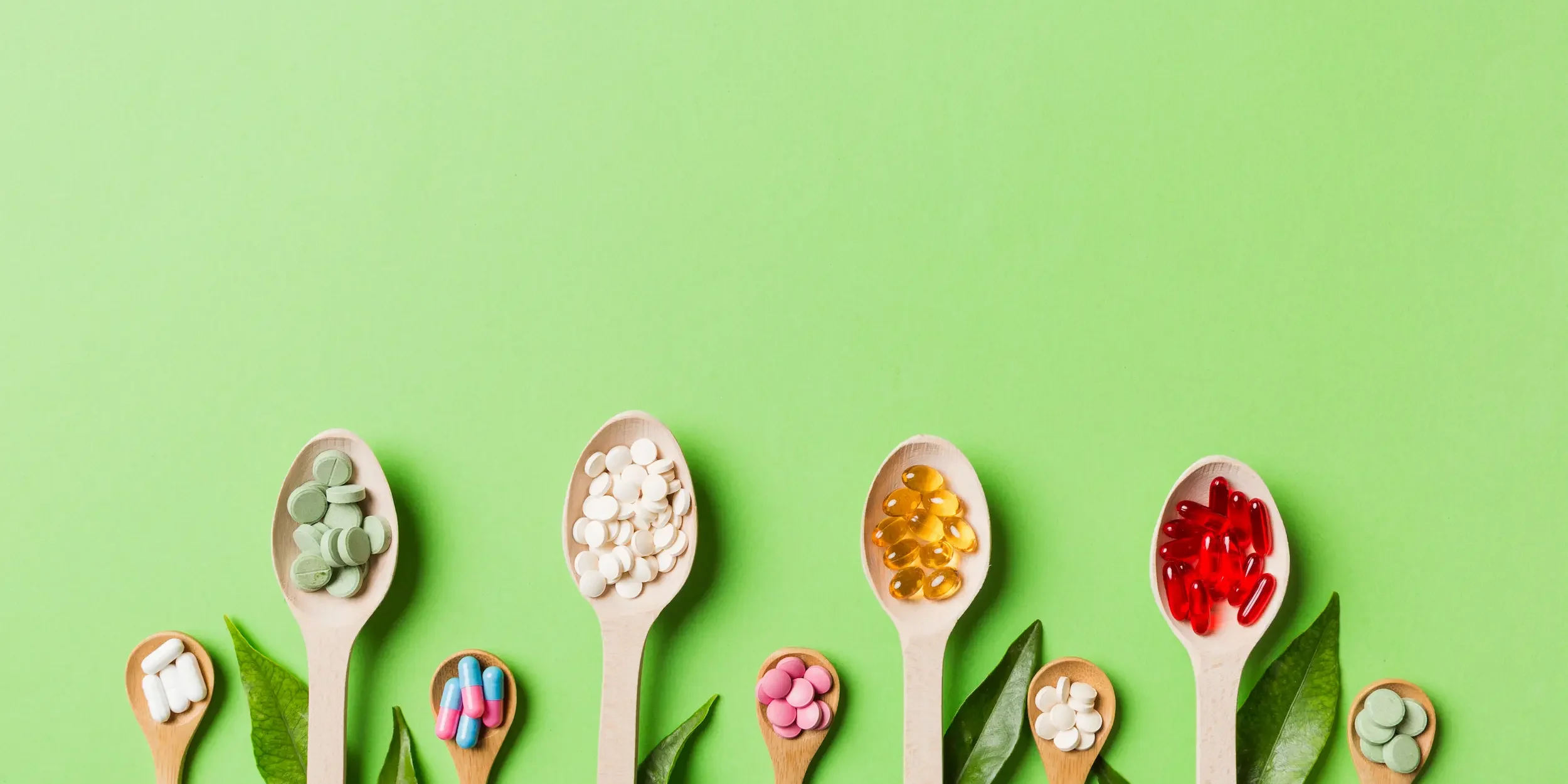 Are mineral supplements worth it A variety of wooden spoons on a green background, each holding different mineral supplements.
