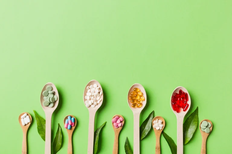 A variety of wooden spoons on a green background, each holding different mineral supplements.
