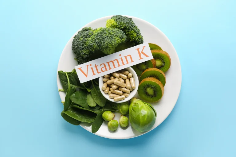 A plate of vitamin K-rich greens around a pot of tablets and a sign reading ‘Vitamin K’.
