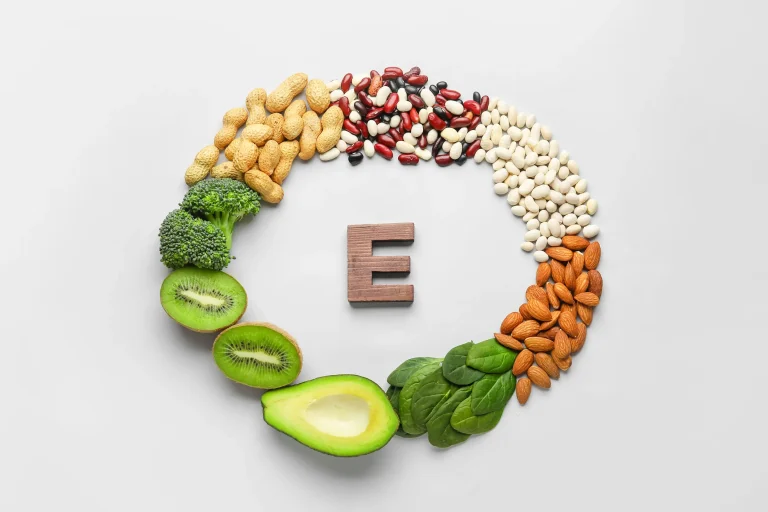 The letter E, surrounded by a circle of vitamin E-rich foods, including nuts and leafy greens.