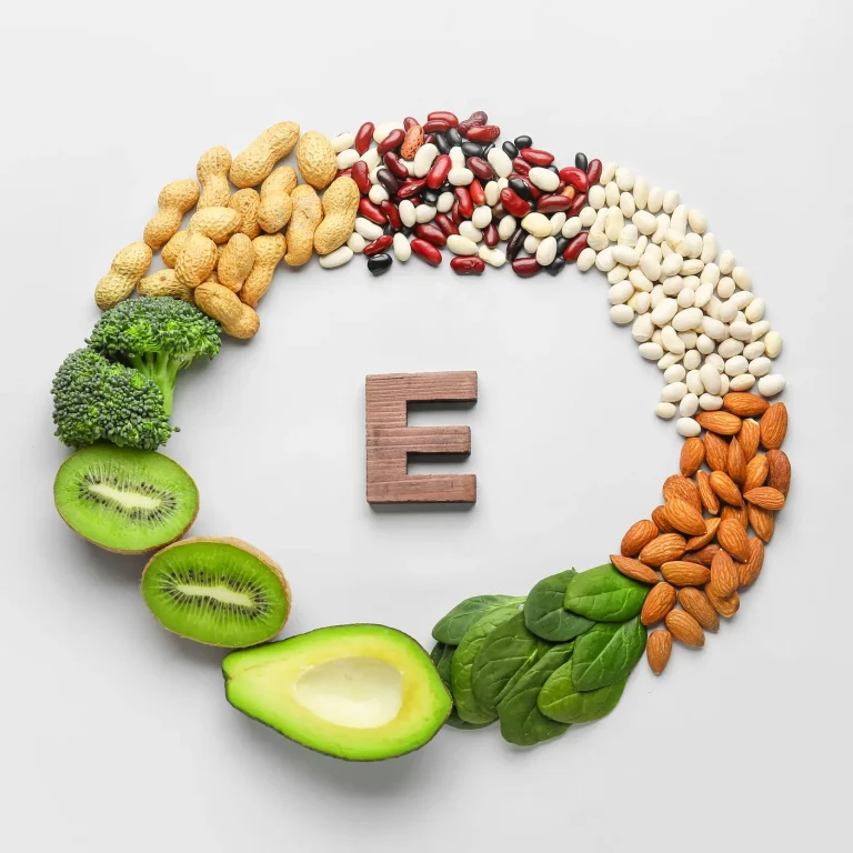 The letter E, surrounded by a circle of vitamin E-rich foods, including nuts and leafy greens.