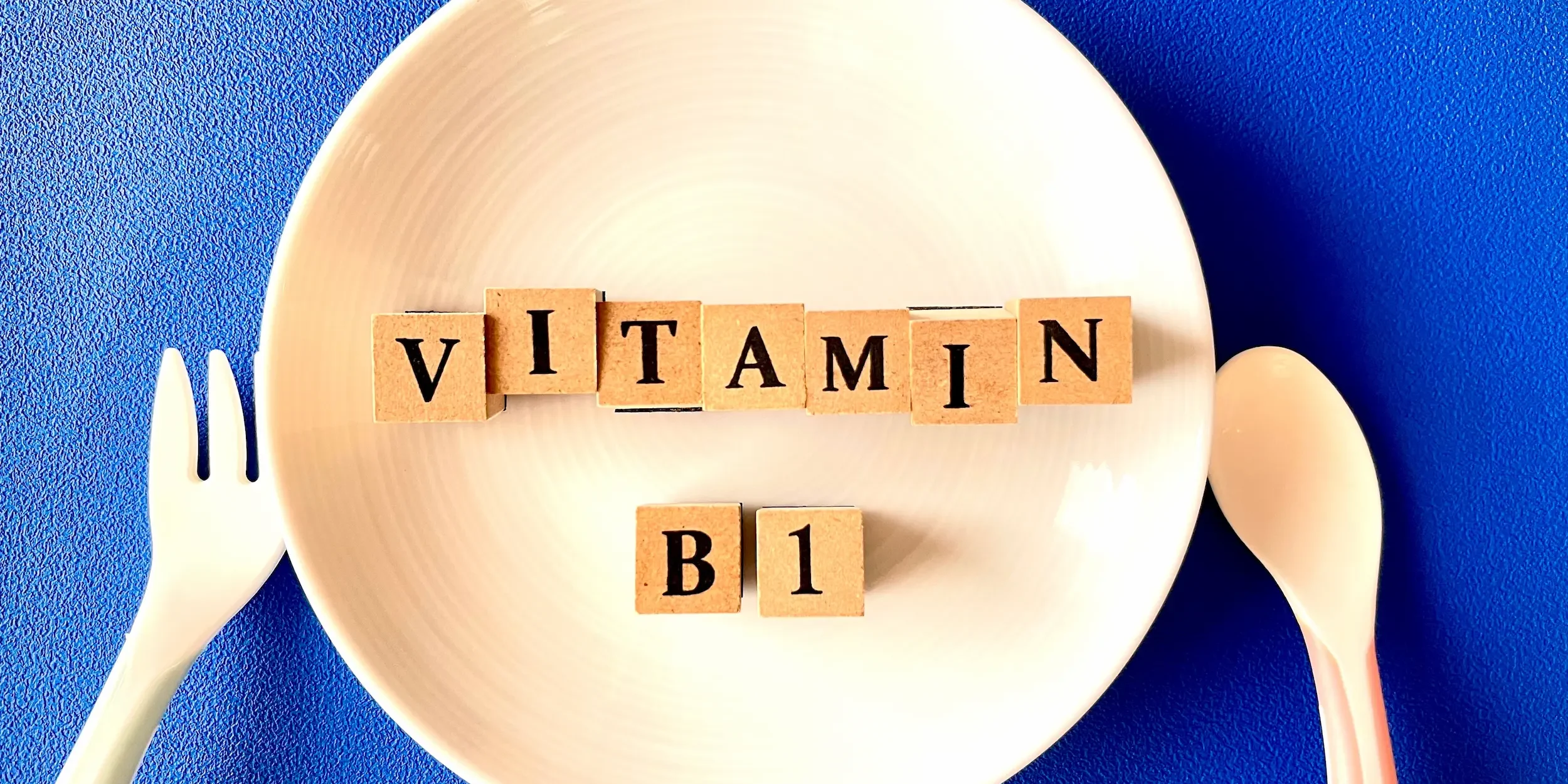 The words ‘Vitamin B1’ spelled on wooden cubes on a dinner plate with cutlery beside it.