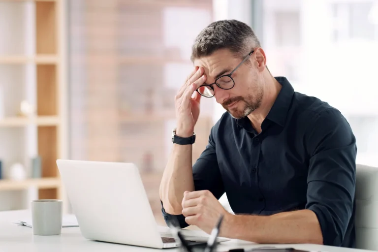 A man experiences a headache while working at a laptop in his office.