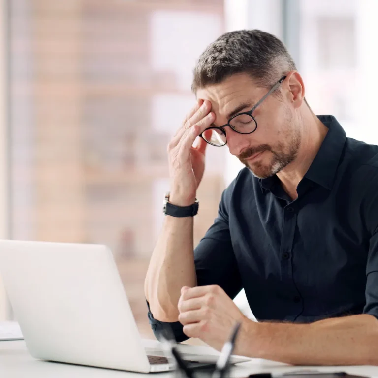 A man experiences a headache while working at a laptop in his office.