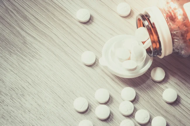 Can you overdose on zinc supplements Pills spill out of a bottle onto a wooden table, representing an excessive dose.