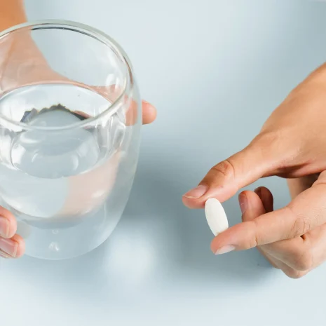 Do zinc supplements have side effects Close-up of a woman’s hands holding a glass of water and a single tablet.