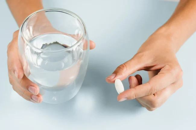 Do zinc supplements have side effects Close-up of a woman’s hands holding a glass of water and a single tablet.