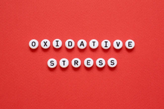 Red background; small, round, white tiles spelling out ‘Oxidative Stress’ in two lines.