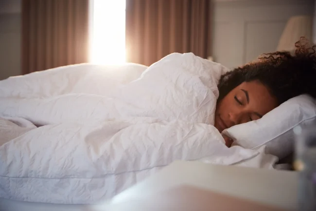 A woman lies in bed fast asleep, despite daylight in the window behind her. A woman lies in bed fast asleep, despite daylight in the window behind her.