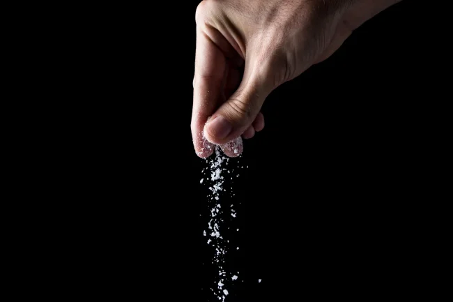 Close-up of a hand sprinkling salt against a black background. Close-up of a hand sprinkling salt against a black background.