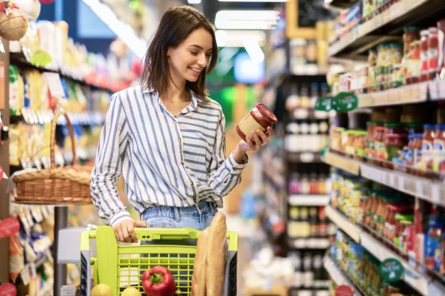 A woman browses a supermarket, checking the nutrition label on a jar of sauce. A woman browses a supermarket, checking the nutrition label on a jar of sauce.