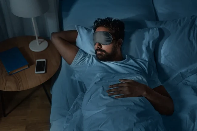 A man lies asleep at night, wearing an eye mask to create a good sleep environment. A man lies asleep at night, wearing an eye mask to create a good sleep environment.
