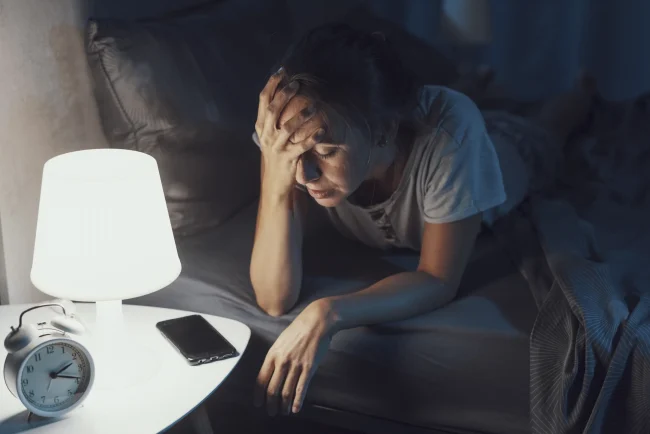 A woman holds her head in bed at night, struggling to sleep. A woman holds her head in bed at night, struggling to sleep.